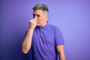 Young handsome modern man wearing casual purple t-shirt over isolated background smelling something...