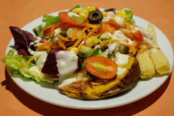 A white plate of salad with assorted vegetables and creamy dressing and an orange table.