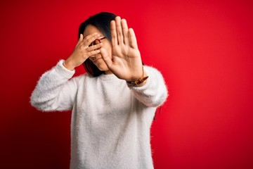 Young beautiful asian woman wearing casual sweater and glasses over red background covering eyes with hands and doing stop gesture with sad and fear expression. Embarrassed and negative concept.