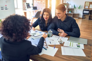 Young beautiful couple applying for mortgage. Sitting smiling happy meeting with real state agent considering mortgage loan at bank