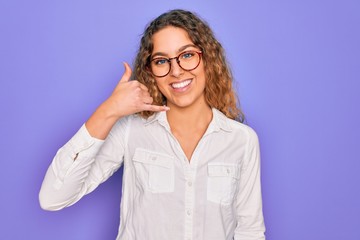 Young beautiful woman with blue eyes wearing casual shirt and glasses over purple background smiling doing phone gesture with hand and fingers like talking on the telephone. Communicating concepts.