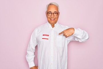 Middle age senior grey-haired man wearing hello my name is introduction sticker with surprise face pointing finger to himself