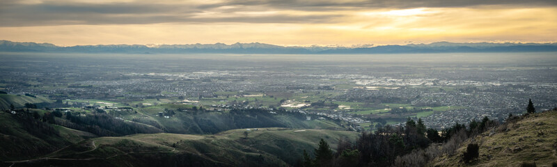 Panoramic sunset shot of city with mountains backdrop. Shot at Port Hills above Christchurch, New Zealand