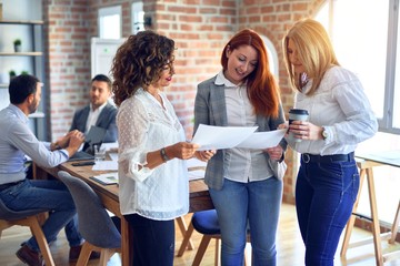 Beautiful businesswomen smiling happy. Standing with smile on face working together reading documents at the office