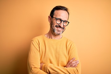 Middle age hoary man wearing casual sweater and glasses over isolated yellow background happy face smiling with crossed arms looking at the camera. Positive person.