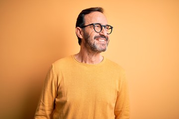 Middle age hoary man wearing casual sweater and glasses over isolated yellow background looking...
