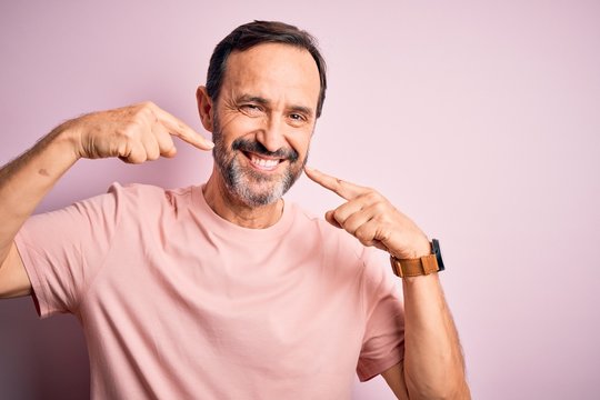 Middle age hoary man wearing casual t-shirt standing over isolated pink background smiling cheerful showing and pointing with fingers teeth and mouth. Dental health concept.