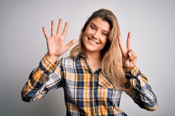 Young beautiful blonde woman wearing casual shirt standing over isolated white background showing and pointing up with fingers number seven while smiling confident and happy.