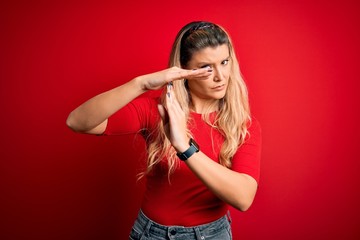 Young beautiful blonde woman wearing casual t-shirt standing over isolated red background Doing...