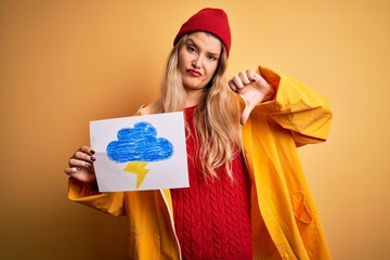 Young beautiful blonde woman wearing raincoat holding banner with cloud thunder image with angry...