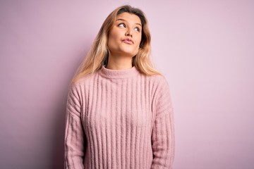 Obraz premium Young beautiful blonde woman wearing casual pink sweater over isolated background smiling looking to the side and staring away thinking.