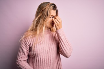Young beautiful blonde woman wearing casual pink sweater over isolated background tired rubbing nose and eyes feeling fatigue and headache. Stress and frustration concept.