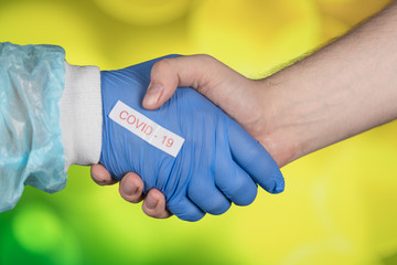 Male hands in a handshake, a hand in medical clothes in blue gloves. COVID pandemic. coronavirus protection