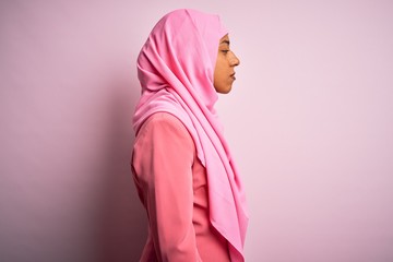 Young African American afro woman wearing muslim hijab over isolated pink background looking to side, relax profile pose with natural face and confident smile.