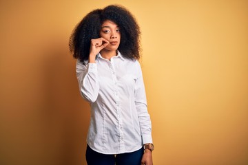 Young beautiful african american elegant woman with afro hair standing over yellow background mouth and lips shut as zip with fingers. Secret and silent, taboo talking