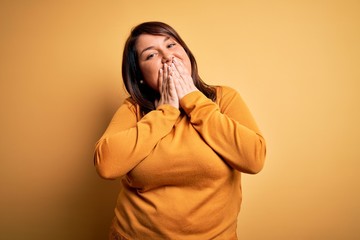 Beautiful brunette plus size woman wearing casual sweater over isolated yellow background laughing...