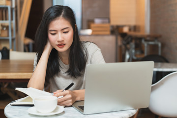Young asian girl studying at home. University Women student learn and research from internet and take a note by e-learning program.