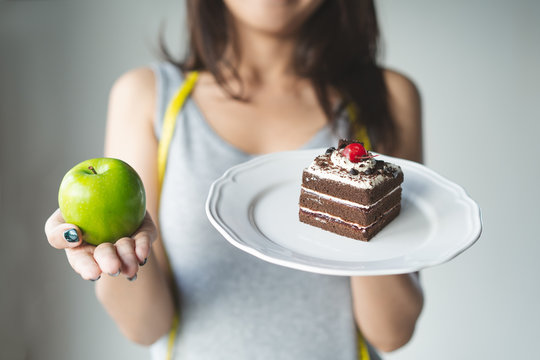 Choose right food for you health. Person eat dessert holding green apple and cake to compare calories as sweet menu to eat during diet.
