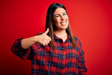 Fototapeta premium Young beautiful woman wearing casual shirt over red background doing happy thumbs up gesture with hand. Approving expression looking at the camera showing success.