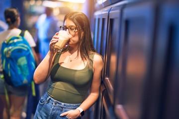 Young beautiful woman leaning on the wall drinking glass of coffee at bar