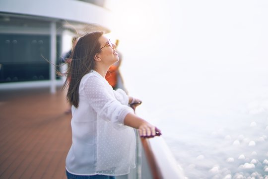 Young beautiful woman on vacation smiling happy and confident. Standing on a deck of ship with smile on face doing a cruise