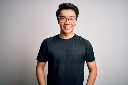 Young handsome chinese man wearing black t-shirt and glasses over white background with a happy and cool smile on face. Lucky person.