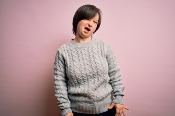 Young down syndrome woman wearing casual sweater over isolated background winking looking at the...