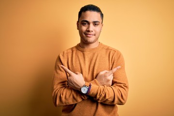 Young brazilian man wearing casual sweater standing over isolated yellow background Pointing to both sides with fingers, different direction disagree