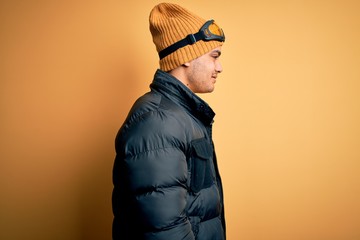 Young brazilian skier man wearing snow sportswear and ski goggles over yellow background looking to...