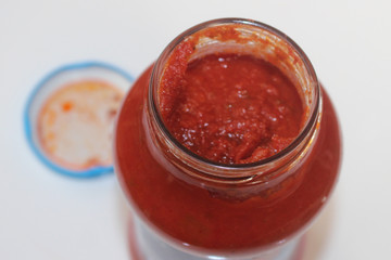 The top of an open jar of tomato pasta sauce. Tomato puree sauce in a jar with the lid in the background