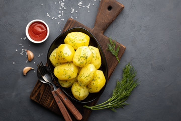 Delicious boiled potatoes with dill in a black plate on a dark background. Top view.
