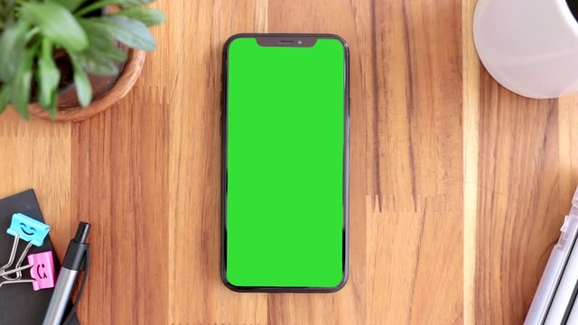 Smart phone place on table wood with green screen, Close-up the cell phone is on the brown desktop with chroma key, Green screen telephone, slider and top view. 