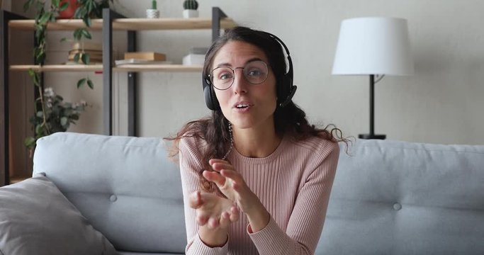Happy young business woman wears headset talks to web camera making distance online video conference call. Female internet teacher doing distant chat working from home. Telework concept. Webcam view