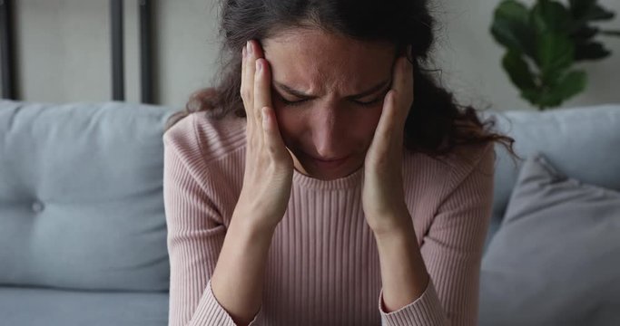 Depressed young woman feels stress concerned about psychological problem sitting alone on sofa at home. Frustrated worried millennial girl suffers from anxiety, despair or shame concept. Close up view