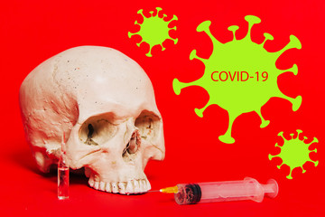 A human skull lies on a red background next to a coronavirus vaccine, an ampule and a syringe with...