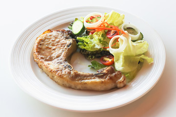 Pork steak with salad in a white plate Place on a white table. The concept of eating cooked food