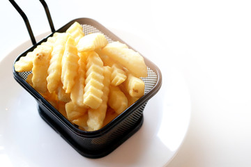 French fries in a black basket Place on a white table. The concept of eating food that causes disease. white background