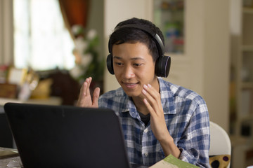 Young asian man talking on laptop camera to communicate with foreign tuitor learning language...