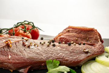 A piece of fresh juicy meat with seasoning and tomatoes on a bright white background.