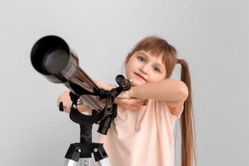 Cute little girl with telescope on light background