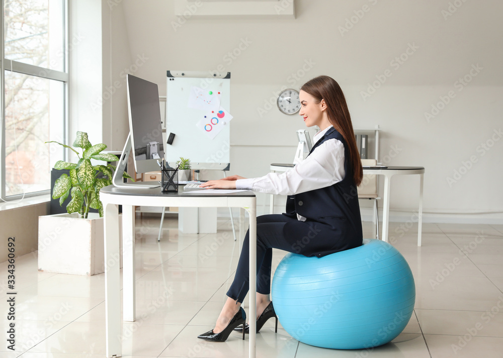 Poster Businesswoman sitting on fitness ball while working in office