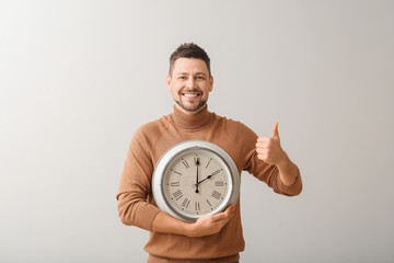 Man with clock showing thumb-up on light background. Time management concept