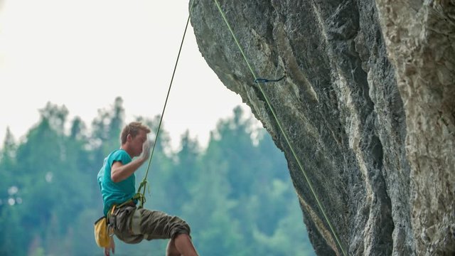 man climbing a vertical cliff reach for an handhold but fails and falls