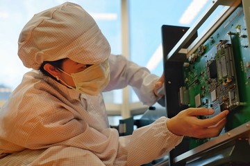 A female electronic manufacturing employee with clean suit (smock), cap and mask inspecting a...