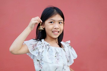 Idiom: Ring a bell. A cute playful Asian girl holding up a small bell by her face, ringing it,...
