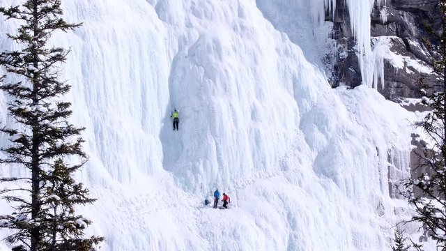 Lead ice climber sets an ice screw to protect steep ascent in dihedral