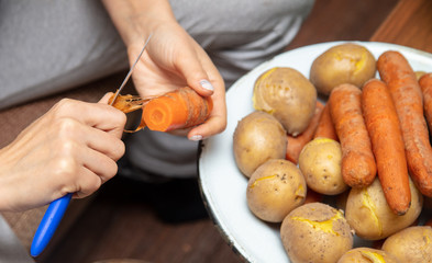 Girl peeling boiled carrots with a knife.
