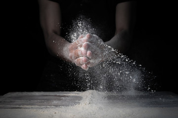 Obraz na płótnie Canvas White flour flies from the hands in air on black background 