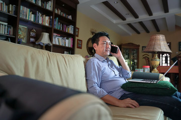 Obraz premium Asian Chinese businessman talking on the cellphone in his house living hall. Work from home concept.
