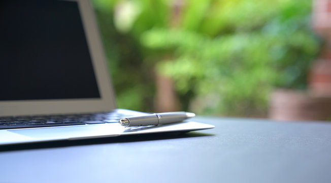 Writing pen on top of computer laptop with green nature background.